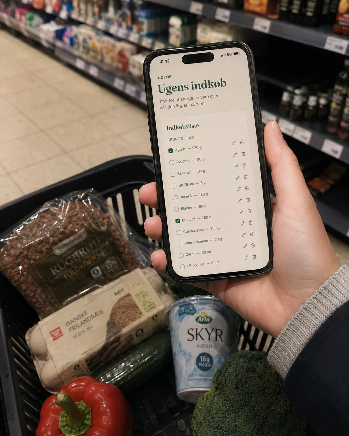 SundPlan indkøbsliste vist på iPhone i et dansk supermarked med rugbrød, æg og skyr i kurven